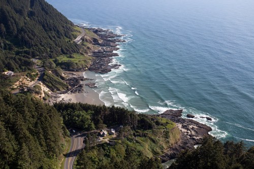 Aerial view of a coastal landscape with rocky shores, waves, and lush green hills along the Oregon coastline.