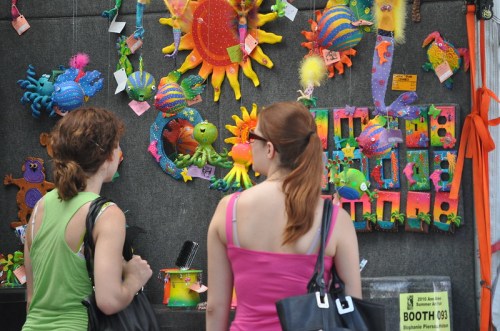 Two women browse colorful, whimsical decorations at a vibrant market stall.