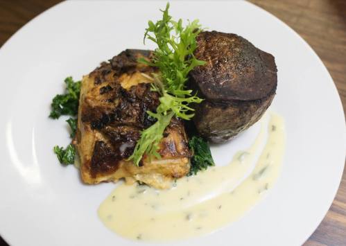 A plated dish featuring grilled fish, a baked potato, and a creamy sauce, garnished with fresh greens.