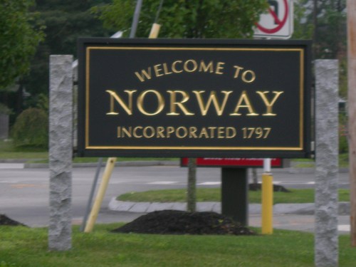 Welcome sign for Norway, established in 1797, with decorative stone pillars and greenery in the background.
