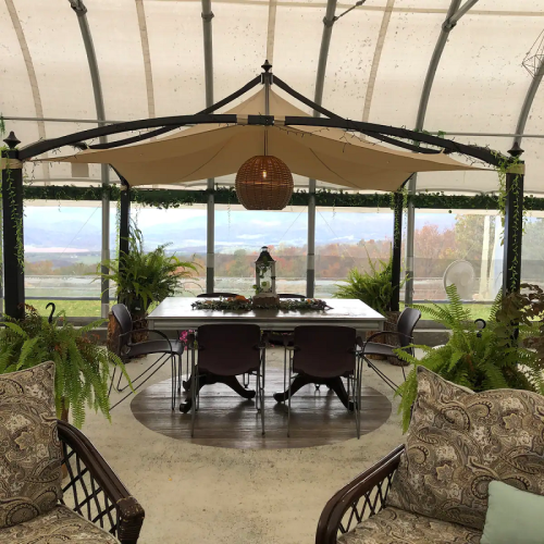 A cozy indoor dining area with a large table, surrounded by plants and comfortable seating, under a canopy.