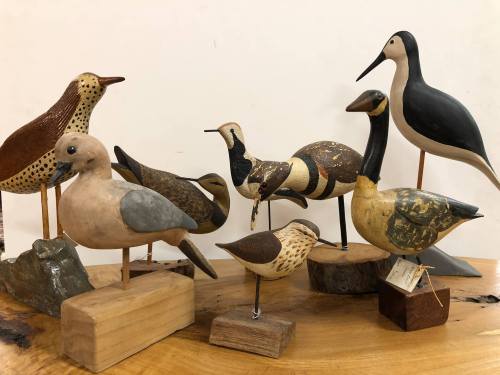 A collection of wooden bird carvings displayed on a table, featuring various species and artistic styles.