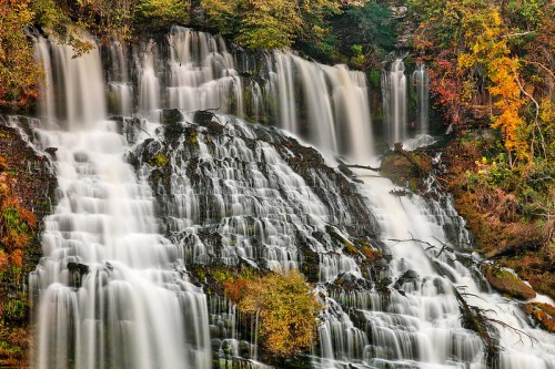 A cascading waterfall surrounded by lush greenery and autumn foliage, creating a serene natural landscape.