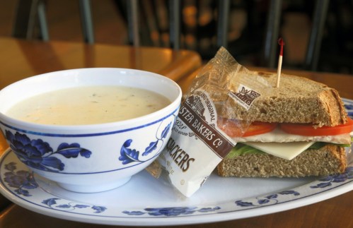 A bowl of creamy soup next to a sandwich with lettuce, tomato, and cheese on whole grain bread, served on a plate.