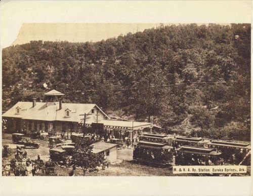 Historic black-and-white photo of a train station in Eureka Springs, Arkansas, with cars and people gathered outside.