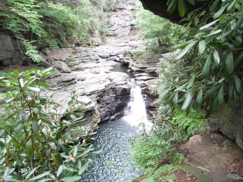 A serene waterfall cascades into a rocky pool, surrounded by lush greenery and steep cliffs.