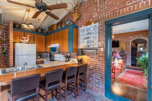 Cozy kitchen with brick walls, wooden cabinets, and a bar area, leading to a warmly decorated living space.