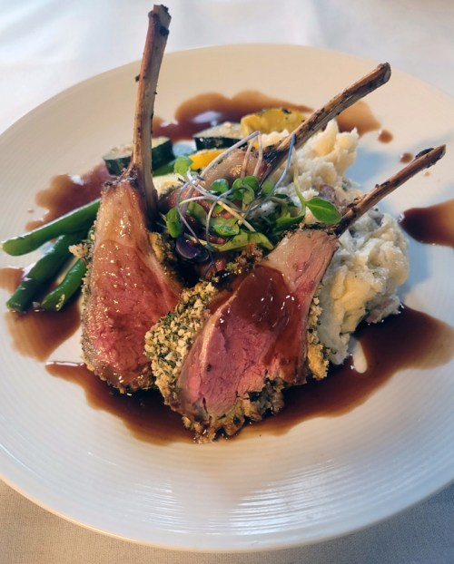 A plate of lamb chops with a herb crust, served with mashed potatoes, green beans, and a rich sauce.