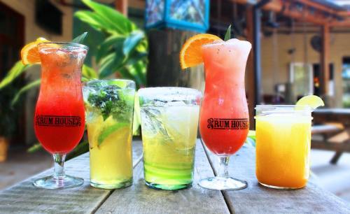 Five colorful cocktails on a table, featuring garnishes like orange and lemon slices, in a tropical setting.
