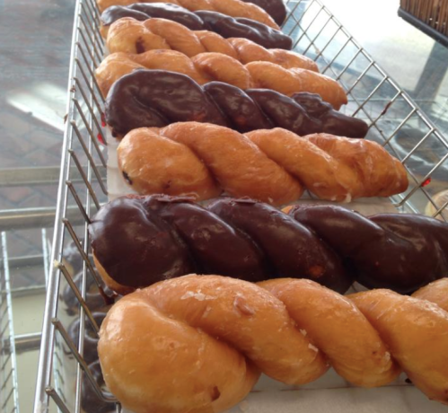 A tray of twisted donuts, some glazed and others coated in chocolate, arranged neatly in a wire basket.