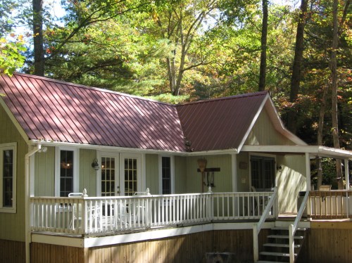 A cozy cabin with a red metal roof, surrounded by trees and featuring a spacious deck.