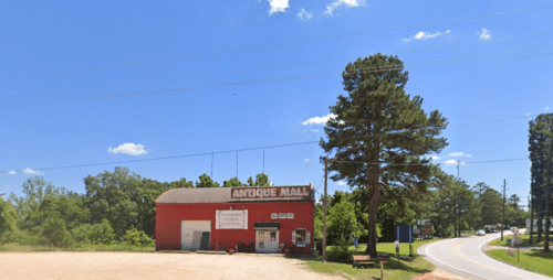 A red antique mall building beside a road, surrounded by trees under a clear blue sky.