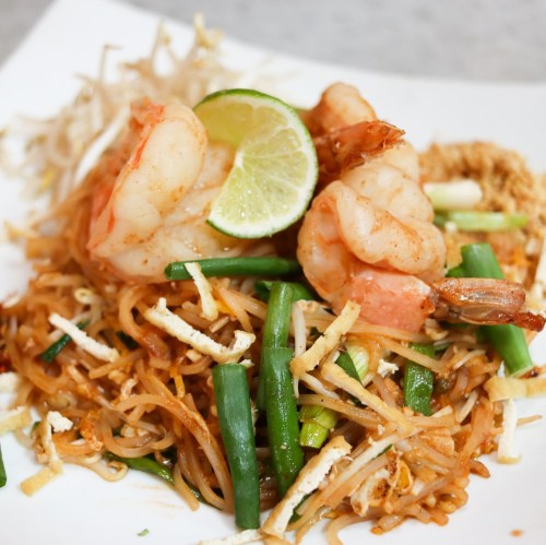 A plate of shrimp pad Thai with lime, green onions, and bean sprouts, garnished with crushed peanuts.