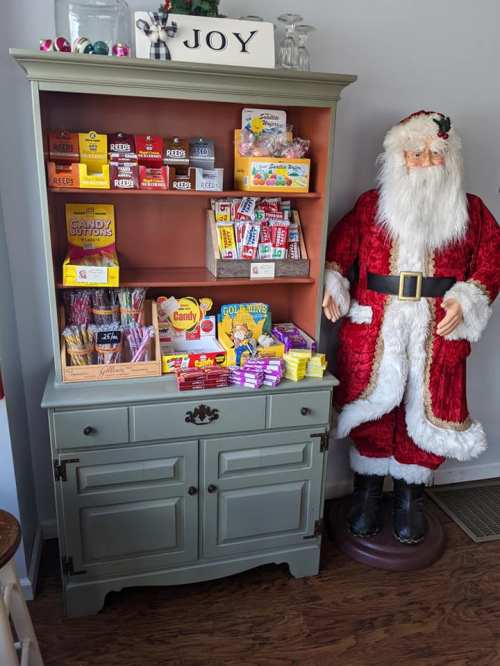 A festive display with a green cabinet filled with candy and a life-sized Santa figure beside it.