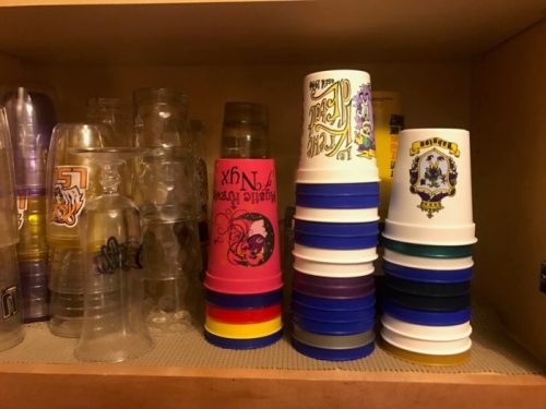 A shelf displaying various plastic cups, including colorful stacked cups and clear glasses.