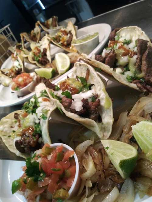 A close-up of tacos filled with beef, onions, and cilantro, served with lime wedges and a side of pico de gallo.