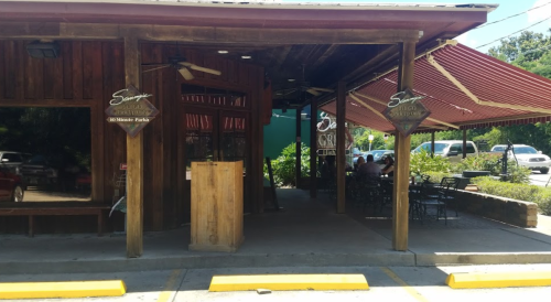 Exterior of a rustic restaurant with wooden features, outdoor seating, and a sign reading "Savor."