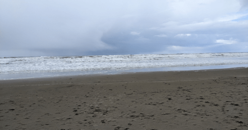 A cloudy beach scene with waves crashing on the shore and a sandy foreground.