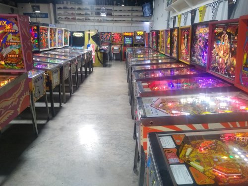 A vibrant arcade filled with rows of illuminated pinball machines in a spacious room.