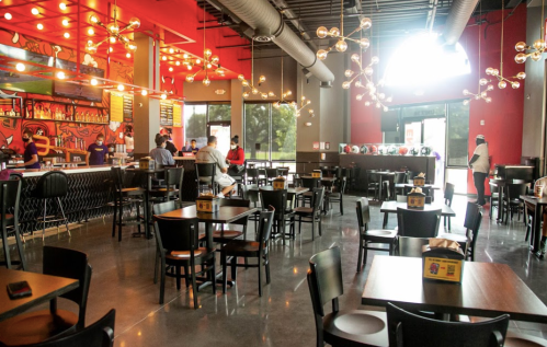 A modern restaurant interior with colorful decor, tables, and a bar area, featuring unique lighting and patrons.