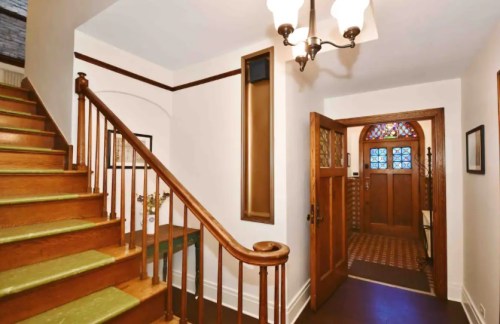 A well-lit entryway with a staircase, wooden accents, and a stained glass door.