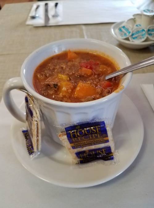 A bowl of hearty soup with vegetables, served with a side of crackers on a white plate.