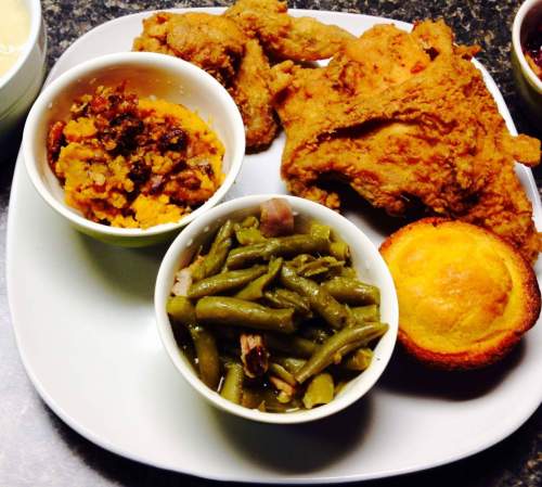 A plate of fried chicken, cornbread, green beans, and sweet potato casserole in small bowls.