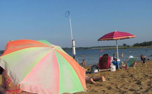 A beach scene with colorful umbrellas, people swimming, and lounging on the sand by a calm lake.