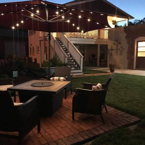 Cozy outdoor seating area with a fire pit, surrounded by a lawn and illuminated by string lights at dusk.