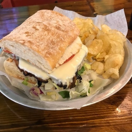 A sandwich with melted cheese, lettuce, and tomato, served with a side of potato chips on a metal plate.