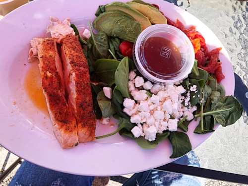 A plate with grilled salmon, spinach, avocado, tomatoes, and a side of dressing.