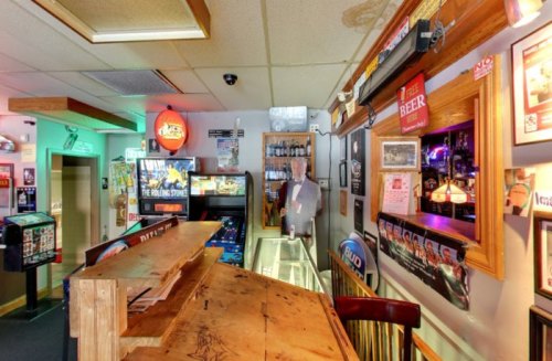 A cozy bar interior featuring a wooden counter, colorful lights, and various framed decorations on the walls.