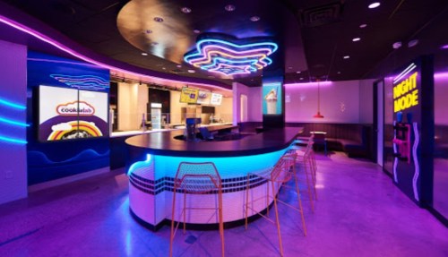 A modern restaurant interior with vibrant neon lights, a curved bar, and colorful digital displays.