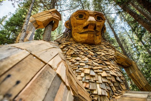 A large wooden sculpture of a troll surrounded by trees, showcasing intricate details in its design and texture.