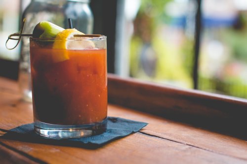A close-up of a cocktail glass with a lemon and lime garnish, resting on a wooden table near a window.