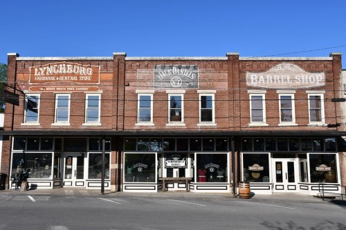 Historic brick storefronts featuring "Lynchburg Hardware & General Store" and "Barrel Shop" under a clear blue sky.