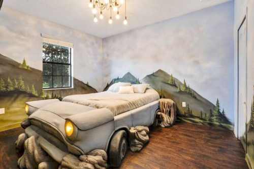 A unique bedroom featuring a bed designed like a car, with mountain-themed wall murals and a cozy atmosphere.