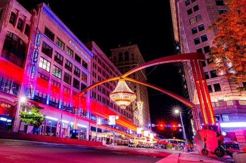 A vibrant city street at night, featuring colorful lights and a large chandelier hanging above the road.
