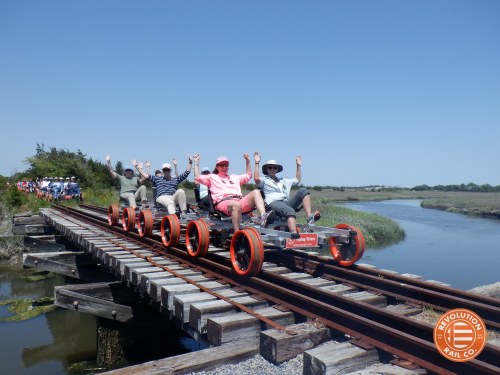 A group of people joyfully riding a rail bike on a wooden bridge over a scenic marshland.