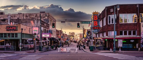 A vibrant street scene with neon signs, cafes, and clubs, under a cloudy sky in a lively urban area.