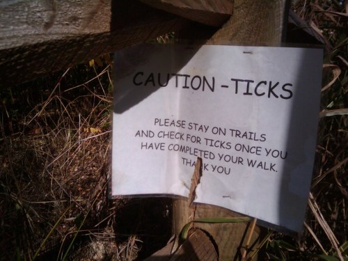 Sign warning about ticks, advising to stay on trails and check for ticks after walking. Thank you message included.