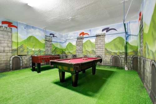 A game room with a pool table and foosball table, featuring castle-themed murals and green carpet.