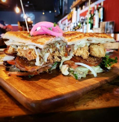 A delicious sandwich with fried chicken, lettuce, tomatoes, and pickled onions, served on a wooden platter.