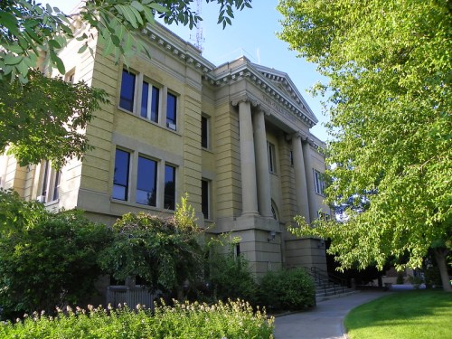 Historic building with columns, surrounded by greenery and trees, under a clear blue sky.