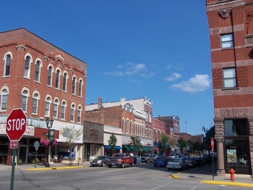 A small town street with historic brick buildings, a stop sign, and parked cars under a clear blue sky.