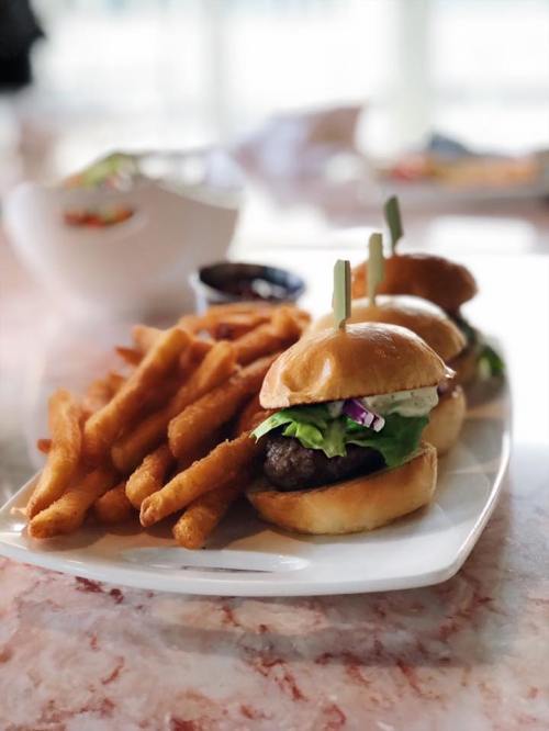 Three mini burgers with lettuce and sauce, served with a side of crispy sweet potato fries.