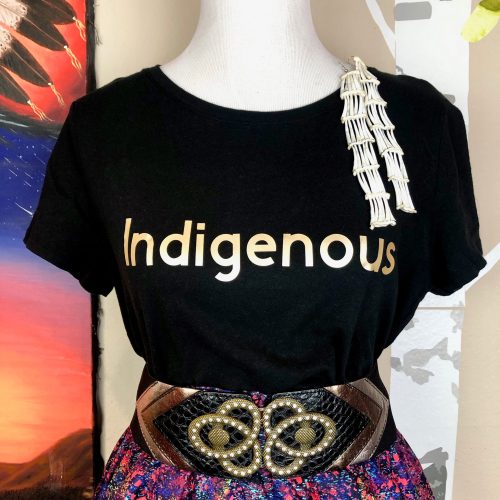 A black t-shirt with the word "Indigenous" in gold, paired with a colorful skirt and a decorative belt.
