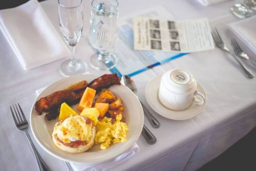 A plate of breakfast with eggs, bacon, fruit, and a coffee cup on a table set with utensils and a menu.