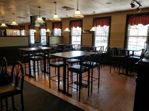Empty restaurant interior with black tables and chairs, wooden floors, and large windows with red curtains.