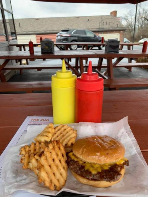 A cheeseburger with melted cheese and waffle fries, accompanied by yellow and red ketchup bottles on a picnic table.
